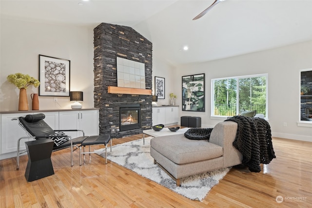 living room featuring light hardwood / wood-style floors, lofted ceiling, and a stone fireplace