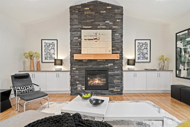 living room featuring a stone fireplace, lofted ceiling, and light wood-type flooring