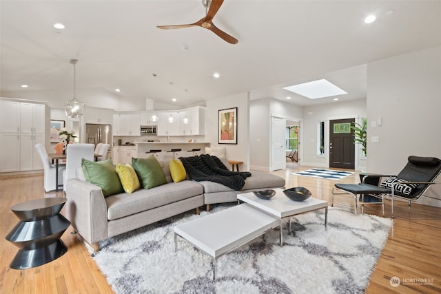 living room with lofted ceiling with skylight, light hardwood / wood-style floors, and ceiling fan