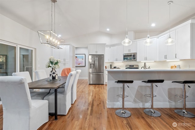 kitchen with light hardwood / wood-style flooring, hanging light fixtures, vaulted ceiling, white cabinets, and appliances with stainless steel finishes