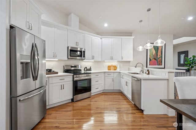 kitchen featuring appliances with stainless steel finishes, white cabinetry, decorative light fixtures, and light wood-type flooring