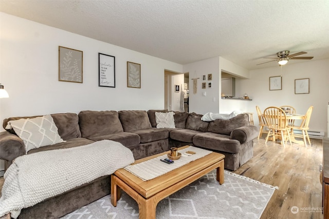 living room with a textured ceiling, ceiling fan, and light hardwood / wood-style flooring