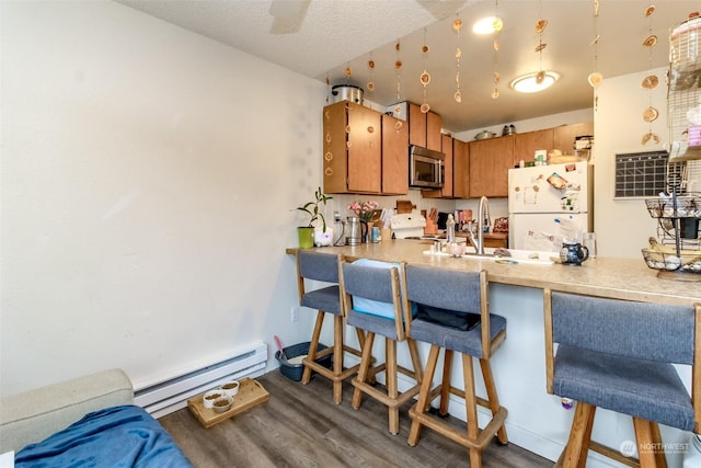 kitchen with sink, white appliances, a breakfast bar area, a baseboard heating unit, and dark hardwood / wood-style flooring