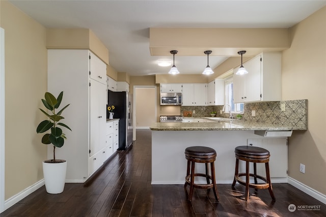 kitchen with light stone counters, white cabinets, kitchen peninsula, stainless steel appliances, and dark hardwood / wood-style floors