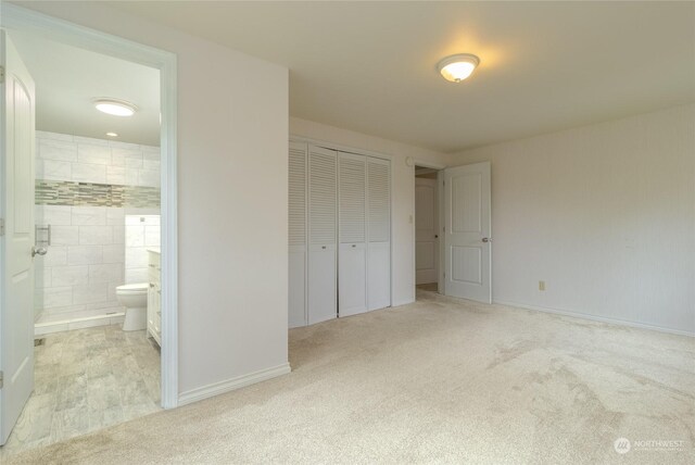 unfurnished bedroom featuring light carpet, ensuite bath, and a closet