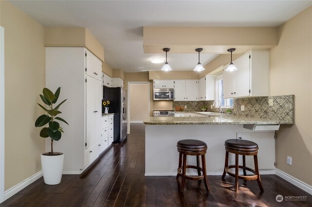 kitchen featuring light stone counters, white cabinets, kitchen peninsula, stainless steel appliances, and dark hardwood / wood-style flooring