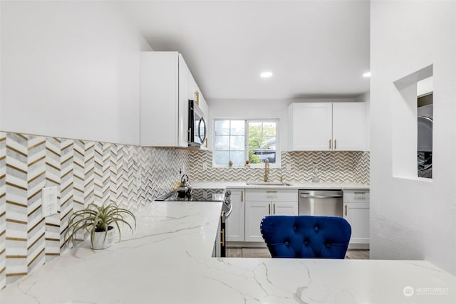 kitchen with appliances with stainless steel finishes, light stone counters, white cabinets, backsplash, and sink