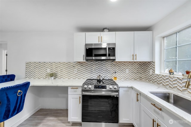 kitchen with tasteful backsplash, white cabinetry, appliances with stainless steel finishes, light stone countertops, and light hardwood / wood-style floors