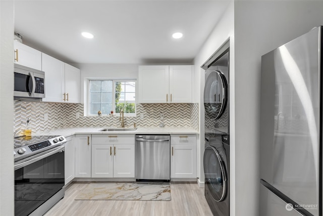 kitchen featuring white cabinets, appliances with stainless steel finishes, sink, and stacked washing maching and dryer