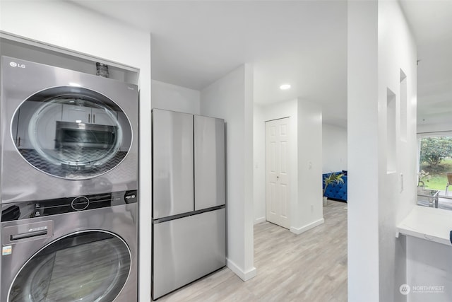 laundry room with light hardwood / wood-style floors and stacked washing maching and dryer