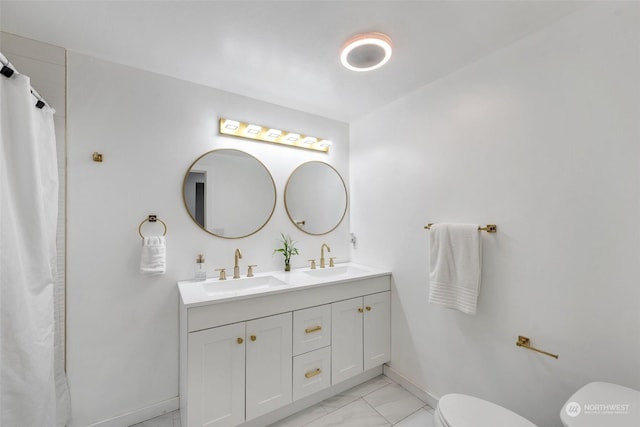 bathroom featuring toilet, marble finish floors, baseboards, and double vanity