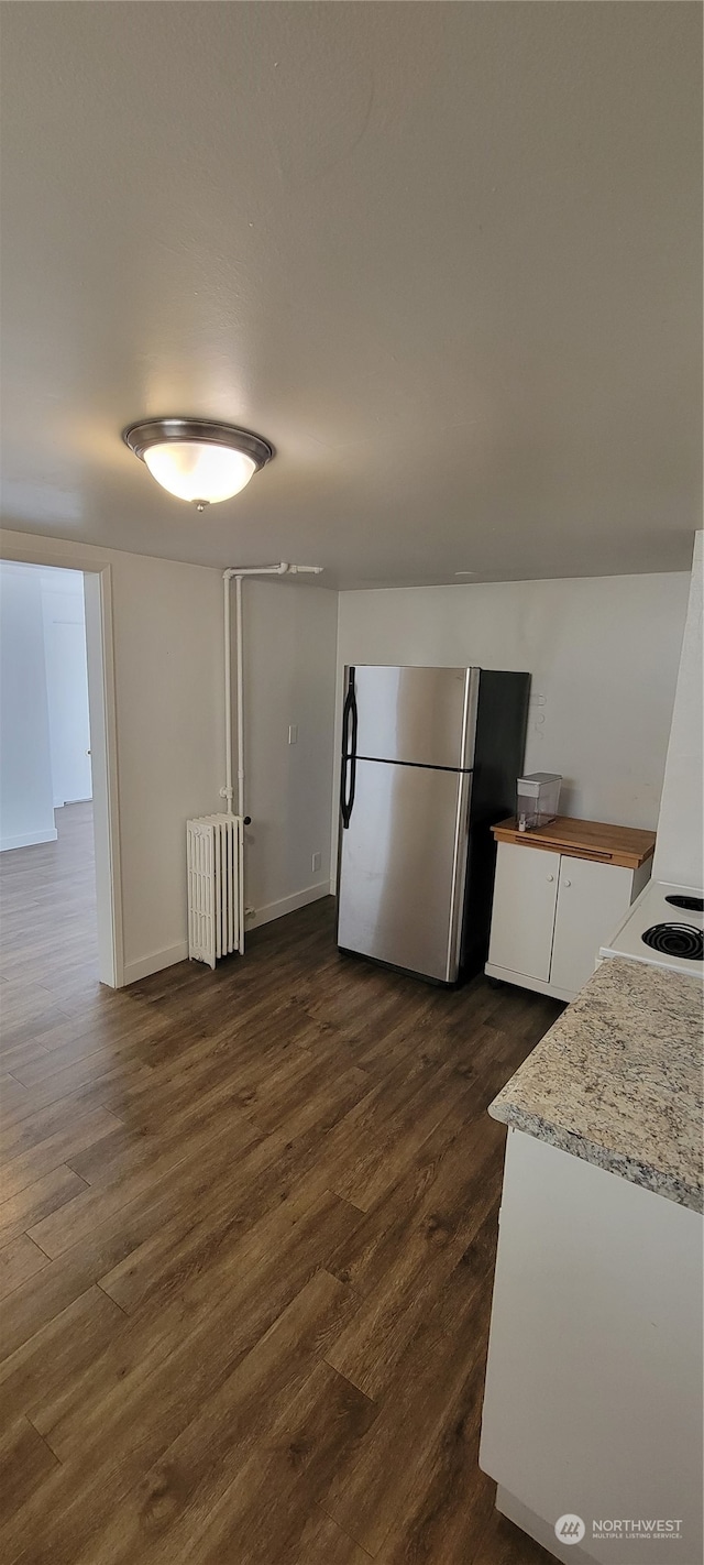 kitchen featuring stainless steel refrigerator, white cabinetry, dark hardwood / wood-style flooring, and radiator heating unit