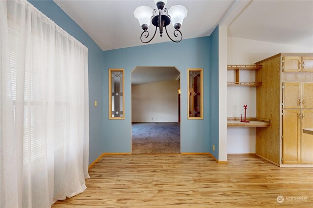 corridor with lofted ceiling, a notable chandelier, and light hardwood / wood-style flooring