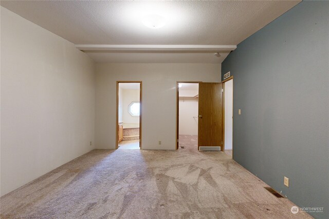 unfurnished bedroom featuring ensuite bathroom, a textured ceiling, a walk in closet, light colored carpet, and a closet