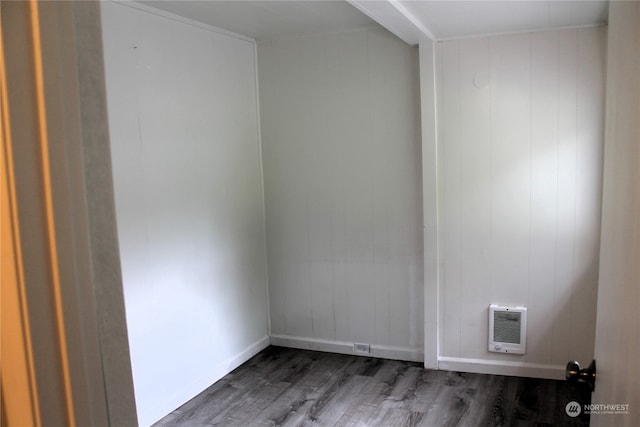 unfurnished room with dark wood-type flooring, wooden walls, and heating unit