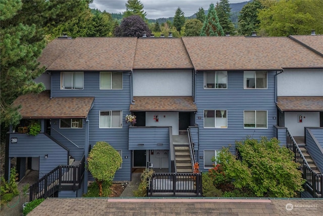 view of property with stucco siding, roof with shingles, fence, and stairs