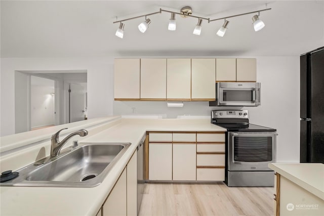 kitchen with light hardwood / wood-style floors, cream cabinets, stainless steel appliances, and sink