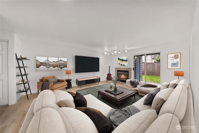 living area featuring baseboards, rail lighting, light wood-style flooring, and a fireplace