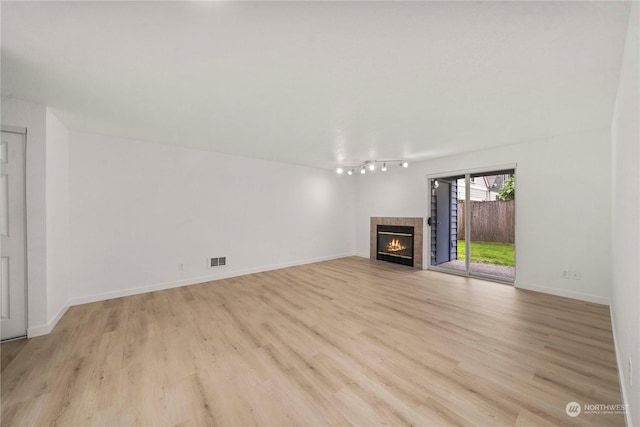 unfurnished living room with light wood-style flooring, visible vents, baseboards, a fireplace, and rail lighting