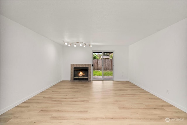 unfurnished living room with a tile fireplace, light wood-type flooring, and baseboards