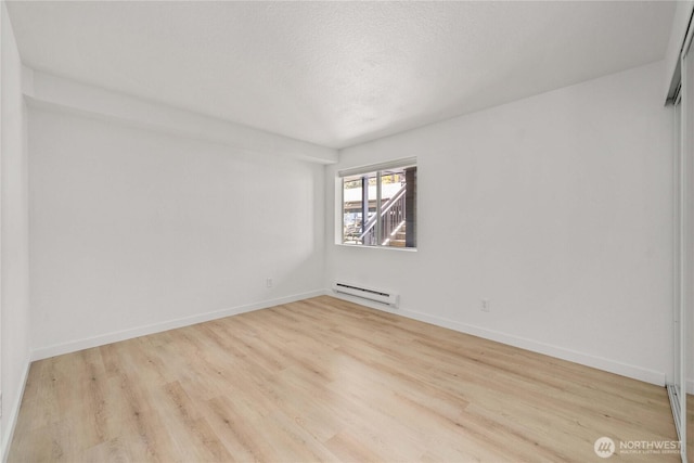 unfurnished room with baseboard heating, wood finished floors, and baseboards