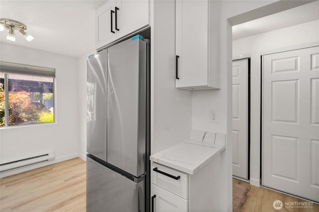 kitchen with light wood finished floors, light stone countertops, white cabinetry, freestanding refrigerator, and a baseboard radiator