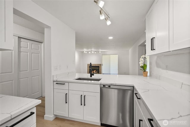 kitchen with stainless steel dishwasher, a sink, white cabinets, and a lit fireplace