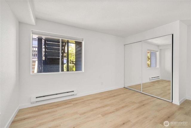 unfurnished bedroom featuring a baseboard heating unit, multiple windows, wood finished floors, and a baseboard radiator