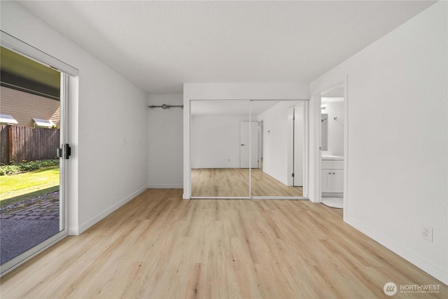 unfurnished bedroom with a closet, ensuite bath, access to exterior, baseboards, and wood finished floors