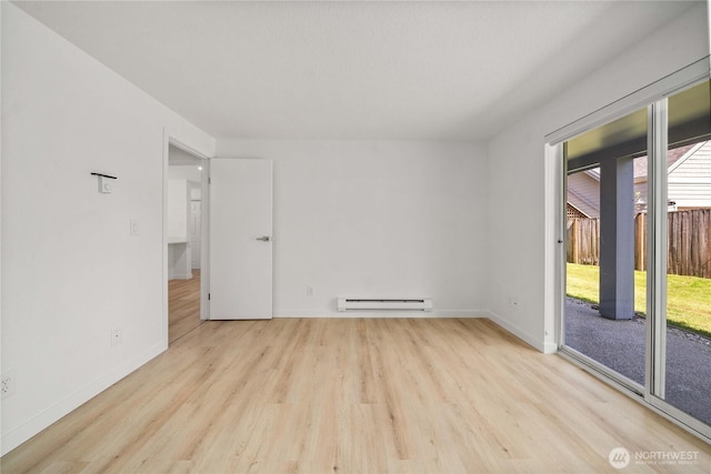 spare room featuring baseboards, baseboard heating, wood finished floors, and a healthy amount of sunlight