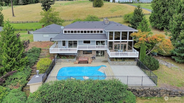 rear view of property featuring a patio, a sunroom, and a fenced in pool