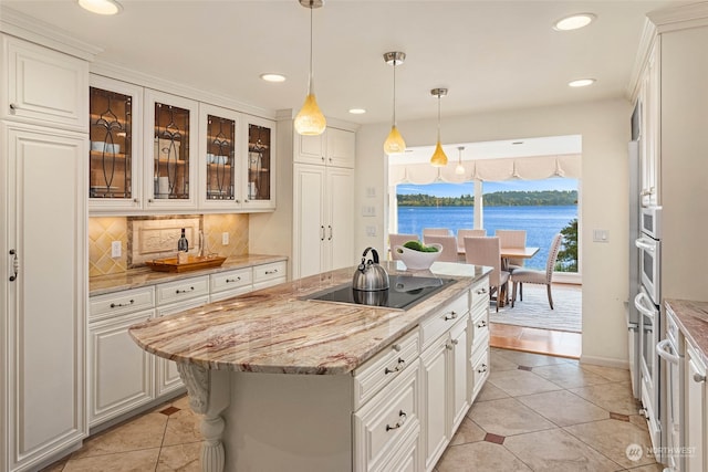 kitchen with an island with sink, white cabinets, backsplash, black electric cooktop, and light stone countertops