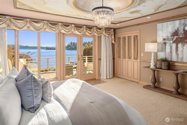 carpeted bedroom with a water view, a tray ceiling, french doors, access to outside, and a notable chandelier