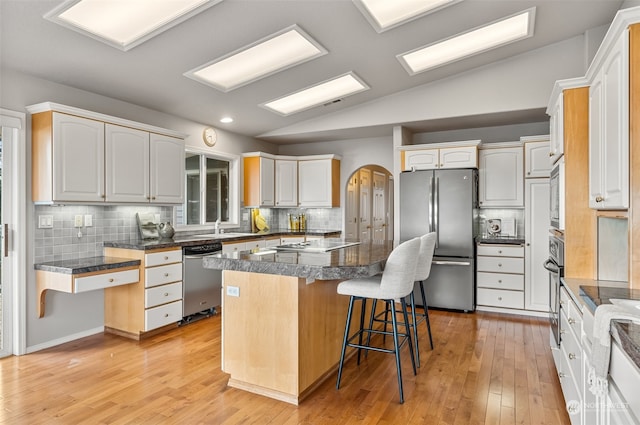 kitchen with a kitchen breakfast bar, vaulted ceiling, white cabinetry, a kitchen island, and stainless steel appliances