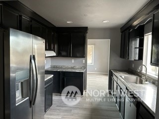 kitchen featuring light stone countertops, sink, light wood-type flooring, and stainless steel refrigerator with ice dispenser