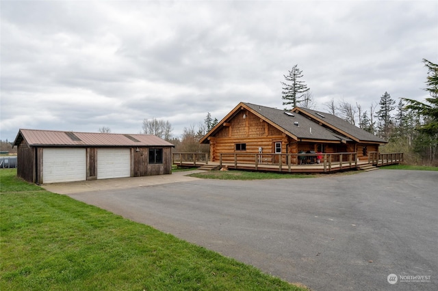 cabin featuring a wooden deck, a front yard, an outbuilding, and a garage