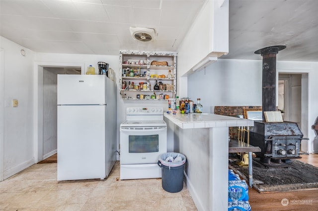 kitchen featuring tile counters, white appliances, and a wood stove