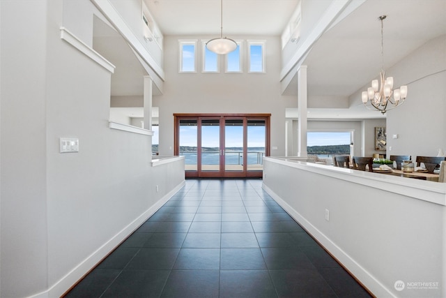 hallway with a water view, a towering ceiling, an inviting chandelier, and dark tile patterned floors