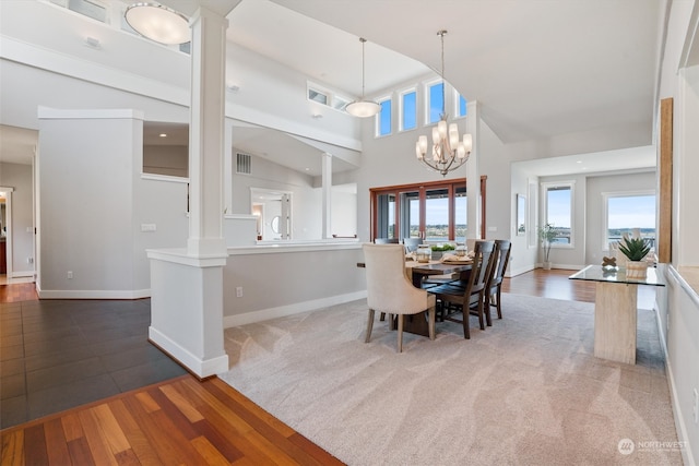 dining space with a towering ceiling, dark wood-type flooring, decorative columns, and a chandelier