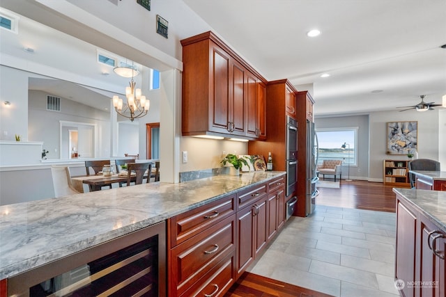 kitchen with light stone countertops, ceiling fan with notable chandelier, wine cooler, and decorative light fixtures