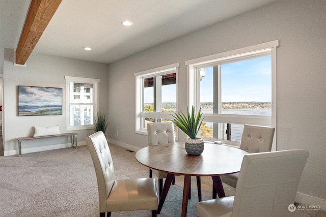 carpeted dining space featuring a water view, a healthy amount of sunlight, and beamed ceiling