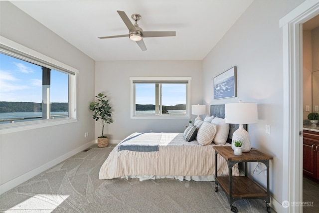 bedroom featuring multiple windows, a water view, light carpet, and ceiling fan