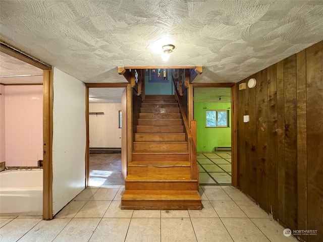 staircase with wooden walls, tile patterned floors, a baseboard heating unit, and a textured ceiling