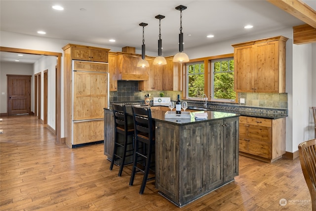 kitchen featuring light wood-type flooring, paneled built in refrigerator, a kitchen island, and pendant lighting