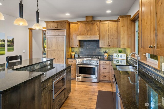 kitchen featuring pendant lighting, dark stone counters, built in appliances, custom exhaust hood, and light hardwood / wood-style flooring