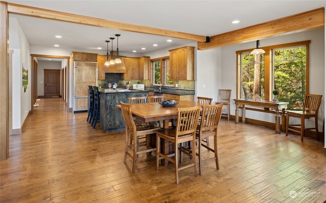 dining space featuring a notable chandelier, sink, light hardwood / wood-style flooring, and beam ceiling