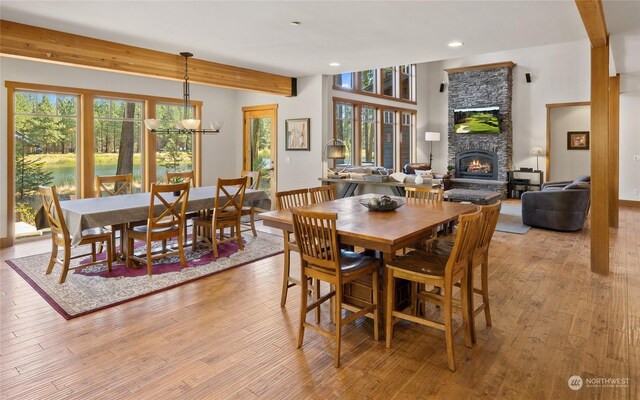 dining space featuring light hardwood / wood-style floors, a stone fireplace, a chandelier, and beamed ceiling