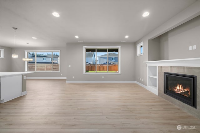 unfurnished living room featuring a tiled fireplace, a chandelier, and light hardwood / wood-style flooring