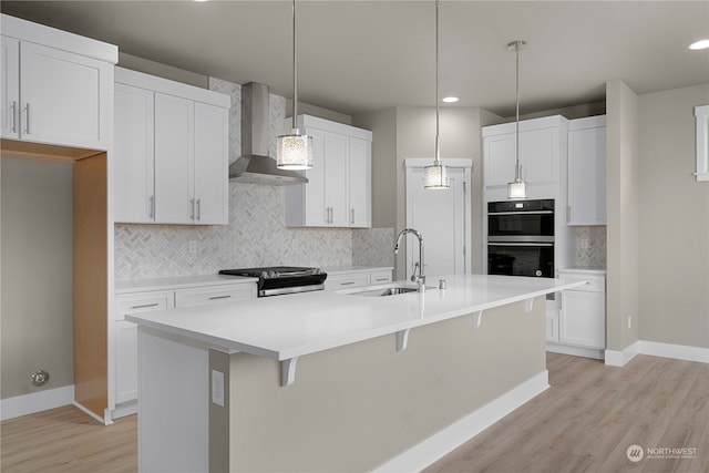 kitchen with wall chimney range hood, decorative light fixtures, sink, stainless steel range, and a kitchen island with sink