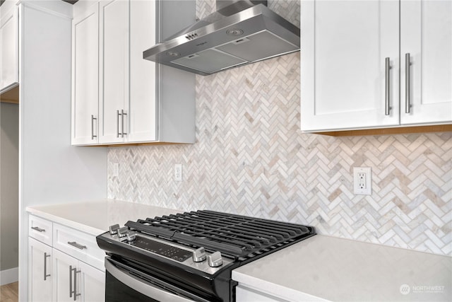 kitchen featuring decorative backsplash, wall chimney range hood, stainless steel gas range, and white cabinets